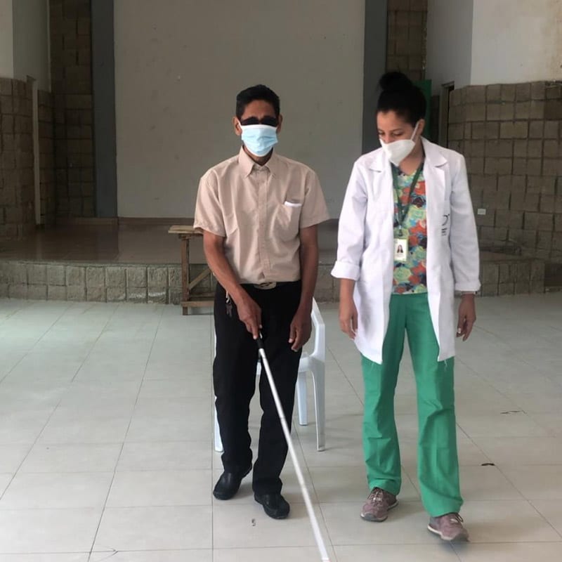 Persona con discapacidad visual con bastón de guía y con profesional de la salud