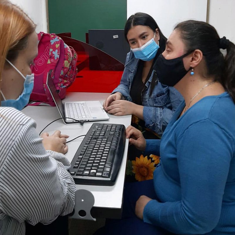 Persona con discapacidad visual aprendiendo a escribir en un teclado de computador junto con dos profesionales de salud