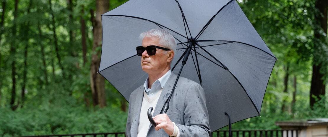 Hombre mayor ciego con paraguas caminando por un parque