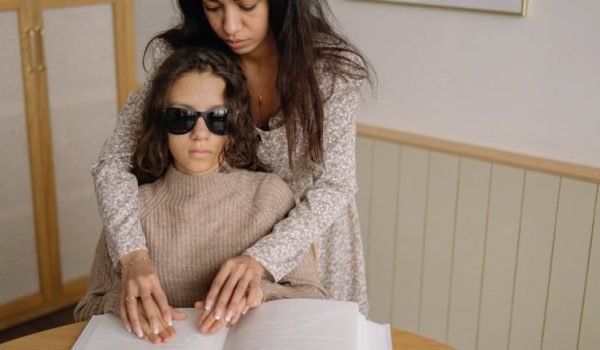 Niña ciega siendo asistida en la lectura de braille
